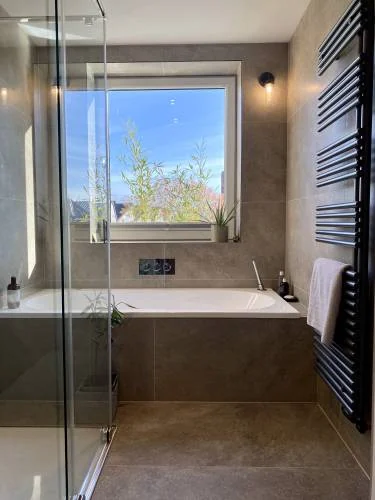 Contemporary bathroom with bath beneath window and black radiator