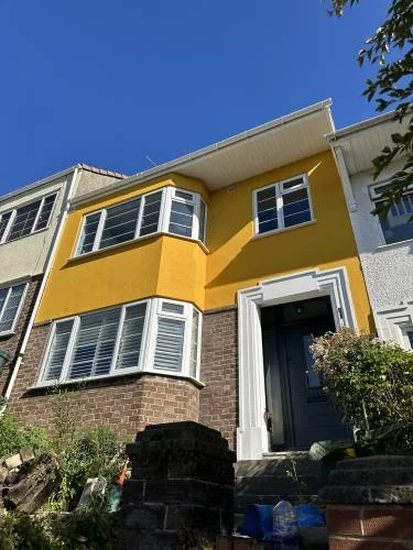 Completed exterior renovation with warm yellow render, bay windows and dark front door